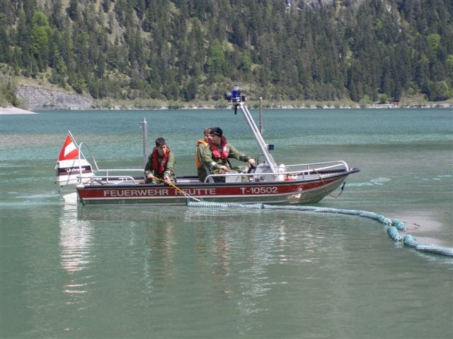Das Boot der Feuerwehr Reutte zieht die Ölsperre über den Plansee