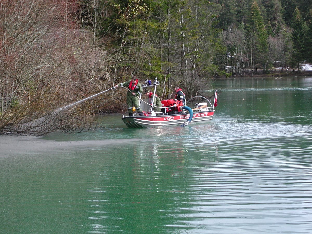 Mittels Feuerwehrboot und Tragkraftspritze werden Ölrückstände aus dem Ufer gewaschen