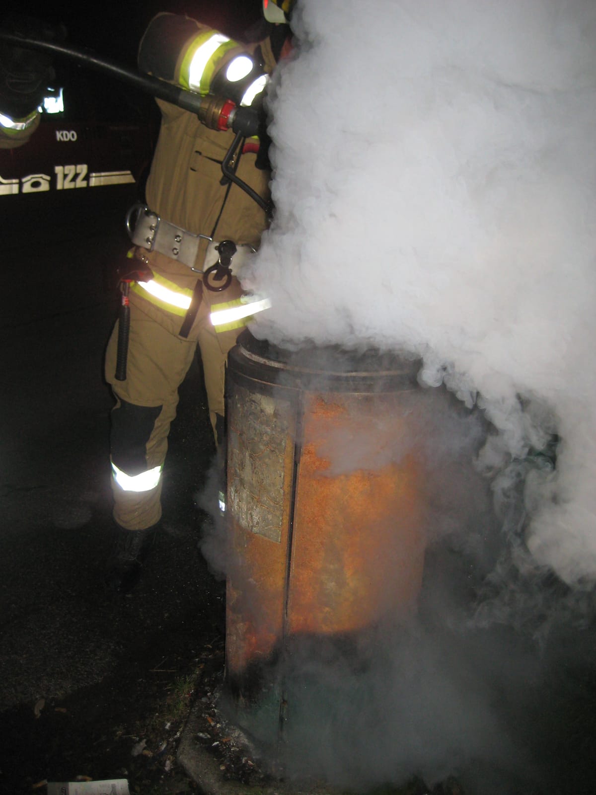 Ein Feuerwehrmitglied löscht die brennende Mülltonne